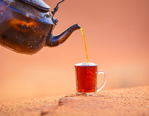 Z čajové konvice se přelévá černý čaj do skleničky na čaj